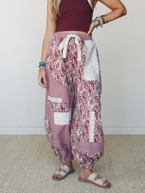 Patchwork harem-style joggers in mauve and paisley steal the show here — styled with a cropped burgundy tank and white sandals, layered with turquoise and beaded bracelets for that effortlessly collected boho feel.