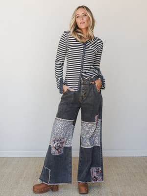 A wide-leg patchwork denim in washed black anchors this outfit — paired with a stripe snap-front cardigan and wood-studded clogs, the whole look has a cool, lived-in 70s energy that feels personal without trying too hard.