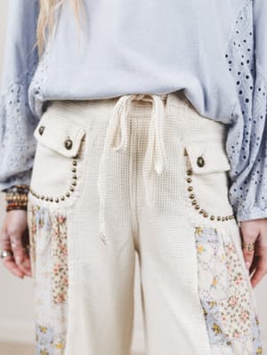 Beige pants with floral patches and decorative buttons worn by a person.