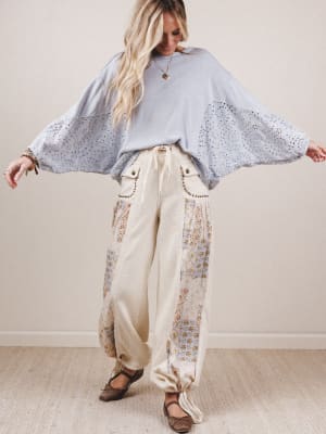 Woman wearing a light blue blouse with bell sleeves and floral pants against a plain background