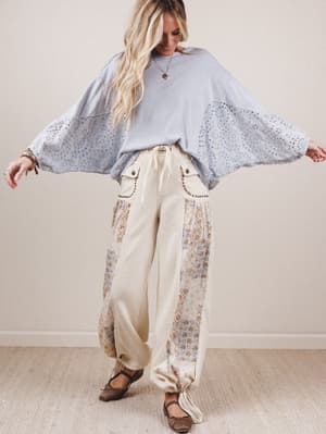 Woman wearing a light blue blouse with bell sleeves and floral pants against a plain background