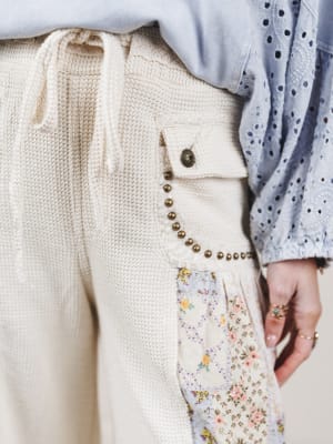 Close-up of a person wearing a cream-colored outfit with a floral pocket detail.