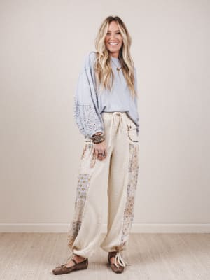 Woman wearing a light blue top and beige pants with floral patterns against a plain background