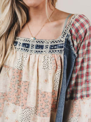 Woman wearing a floral dress with a plaid shirt over it, standing against a neutral background.