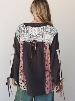 A patchwork boho blouse shot from behind, mixing charcoal gauze, black-and-white paisley bandana print, and blush floral panels with lace trim details — the kind of top that looks like it has a whole personality before you even turn around.