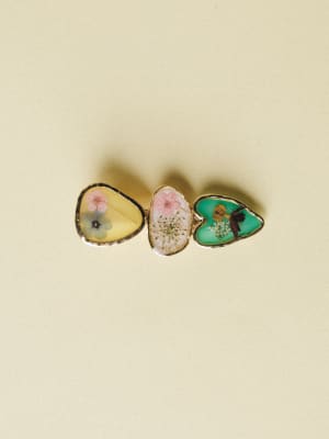 Three freeform resin hair clips arranged in a row, each encasing pressed flowers against a soft yellow, blush, and mint background — the kind of piece that feels like a little garden you can wear.