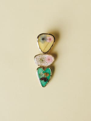 A stacked three-piece resin hair clip with pressed botanicals sealed inside each segment — soft yellow and pink florals up top, lacy Queen Anne's lace in the middle, and a teal heart-shaped charm at the base — all set in a silver-toned frame against