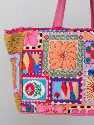 A vibrant canvas tote bursting with patchwork-style printed panels, embroidery, mirror embellishments, and woven raffia sides — the kind of bag that looks like it has a whole personality before you even pack it.