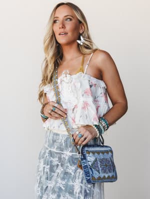A sun-kissed boho look built around layers of texture — a floral ruffle cami over a lace-embroidered sheer skirt, anchored by a beaded denim crossbody bag and stacked with turquoise jewelry that feels collected, not coordinated.