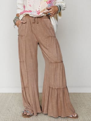 Tiered wide-leg pants in a washed mocha tone styled with a cream graphic top and stacked turquoise bracelets — the kind of effortless, flowy bottom that lives between cozy and put-together.