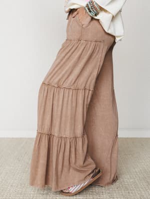 Tiered wide-leg pants in a soft mocha mineral wash, styled with a cream oversized top, stacked beaded bracelets, and floral sandals — the kind of outfit that looks effortless but clearly wasn't an accident.