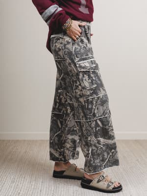 Person wearing camouflage pants and sandals on a plain background