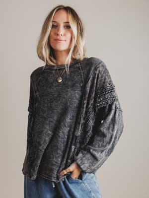 Woman wearing a dark gray distressed top with lace details on a plain background