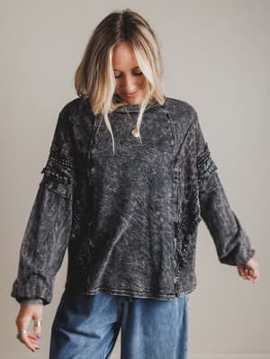 Woman wearing a distressed black sweater and blue jeans against a plain background
