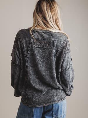 Person wearing a black acid-wash top and blue jeans against a beige background