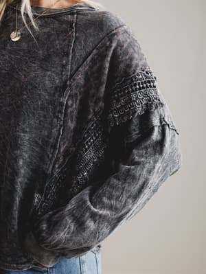 Black distressed denim top with embroidered sleeves on a neutral background