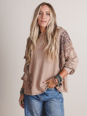 Woman wearing a beige sweater with leopard print sleeves and blue jeans on a plain background