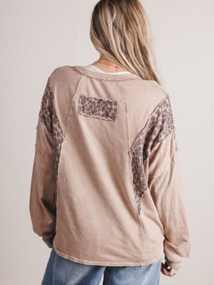 Person wearing a beige long-sleeve shirt with leopard print accents on a plain background