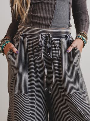 Person wearing a brown ribbed sweater and striped pants with a neutral background