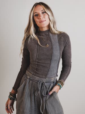 Woman wearing a brown ribbed sweater and striped pants against a plain background