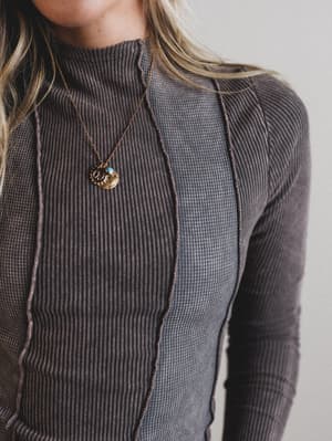 Person wearing a dark ribbed sweater with a necklace against a neutral background