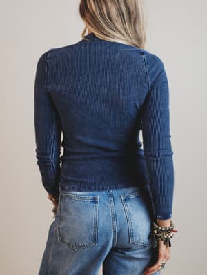 Person wearing a blue ribbed sweater and jeans against a neutral background