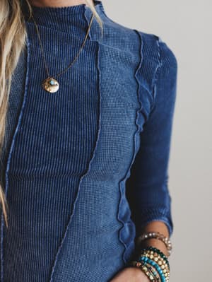 Close-up of a person wearing a blue ribbed sweater with ruffled details, accessorized with a necklace and bracelets.