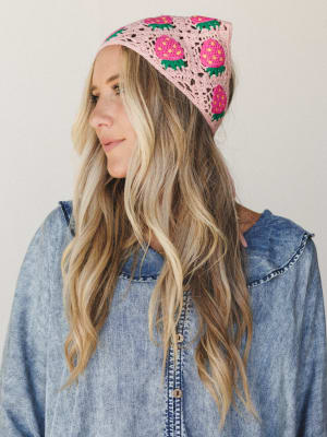 A crochet strawberry headband in blush pink sits on a model with wavy blonde hair, paired with a soft chambray button-down — the kind of accessory that makes a whole outfit feel intentional without trying too hard.