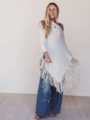 Woman wearing a white fringe top and blue jeans with a star design.