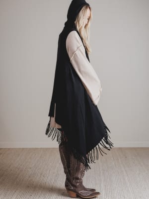 Person wearing a black fringed vest with a plain background