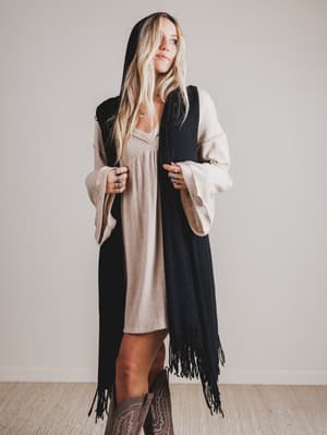 Woman wearing a long black hooded vest and beige dress with a plain background