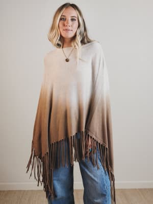 Woman wearing a gradient poncho with fringes against a plain background