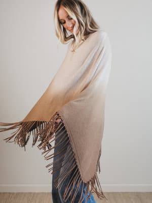Woman wearing a beige poncho with brown fringes against a plain background