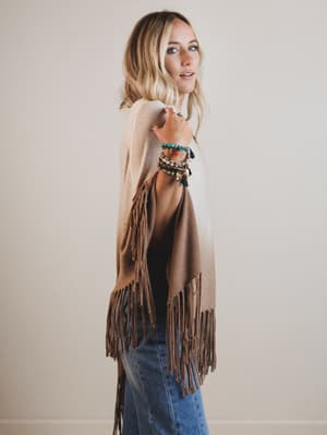 Woman wearing a beige fringe poncho with a plain background