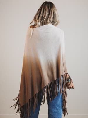 Woman wearing a gradient poncho with fringes on a plain background