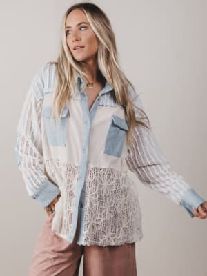 Woman wearing a layered outfit with a lace top and denim jacket against a plain background