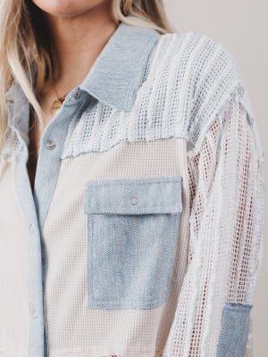 Person wearing a light blue denim shirt with a white knit cardigan over it.