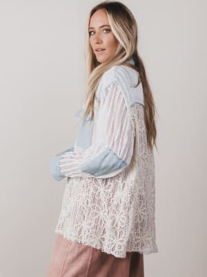 Woman wearing a white lace top with blue accents on a plain background
