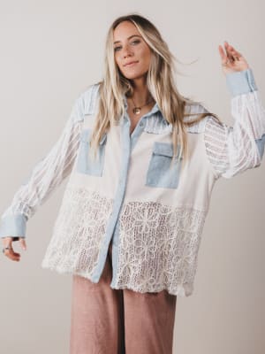 Woman wearing a light blue denim shirt with lace sleeves and hem against a plain background