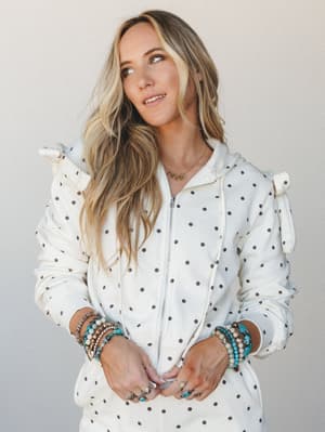 A cream polka dot zip-up hoodie styled with an armful of boho bracelets and a 'MAMA' letter necklace — the kind of cozy, collected look that feels just as intentional as it does effortless.