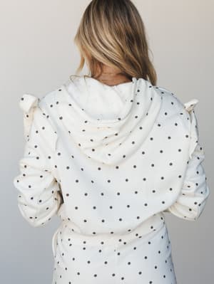 A back-facing shot of a cream polka dot hoodie with ruffle shoulder details and a coordinating tie-waist bottom — cozy and a little sweet, like your favorite lazy Sunday outfit got a thoughtful upgrade.