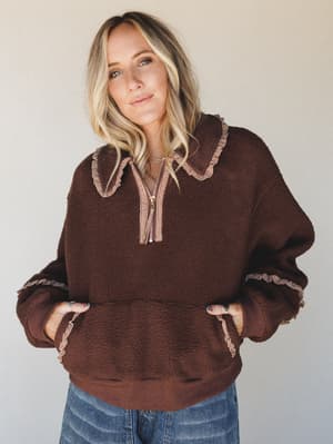 A cozy sherpa pullover in deep chocolate brown with gingham ruffle trim at the collar, cuffs, and kangaroo pocket — the kind of piece that makes a Tuesday feel intentional.