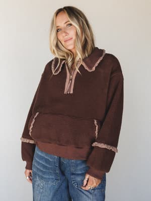 A cozy sherpa half-zip pullover in deep chocolate brown with gingham ruffle trim at the collar, cuffs, and pocket — styled with relaxed wide-leg denim for that perfectly lived-in fall feeling.