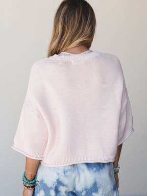 A back-view shot of a boxy cropped knit sweater in the softest blush pink, layered over a printed top and paired with tie-dye bottoms — the kind of effortless combo that looks accidental but really isn't.