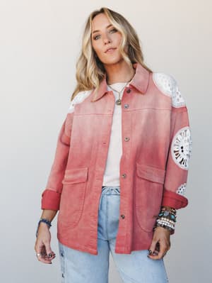 A relaxed, lived-in shacket in washed terracotta pink with bold white crochet medallion panels at the shoulders and sleeves — styled over a simple white tee and light-wash jeans with layered boho jewelry for an effortlessly expressive everyday look.