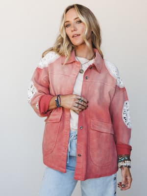 A relaxed, sun-washed shacket in dusty coral with crochet lace inserts at the shoulders and sleeves, layered over a white tee and light wash jeans — the kind of outfit that looks like it came together effortlessly but you definitely thought about it.