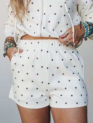 A cropped mid-shot of a matching polka dot set — a zip-up hoodie and relaxed pull-on shorts in cream — styled with stacked turquoise and silver boho jewelry for a comfy-cool, put-together-without-trying vibe.