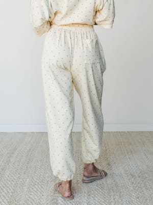 A back-view shot of a matching polka dot set — relaxed jogger pants with a cropped sweatshirt — in a soft butter yellow with powder blue dots, styled with strappy flat sandals for an effortlessly cozy, put-together feel.