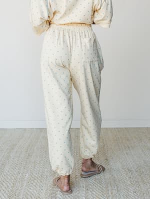A back-view shot of a matching polka dot set — relaxed jogger pants with a cropped sweatshirt — in a soft butter yellow with powder blue dots, styled with strappy flat sandals for an effortlessly cozy, put-together feel.