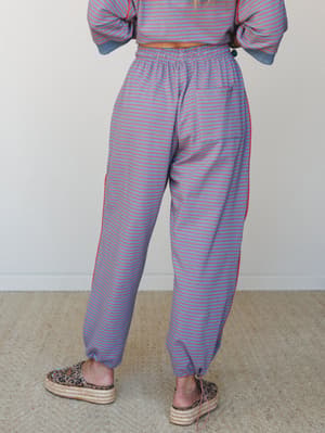 A back-facing model wears relaxed striped pants in dusty blue with fine red stripes, paired with a matching cropped sweatshirt and leopard print platform espadrilles — casual and a little unexpected in the best way.